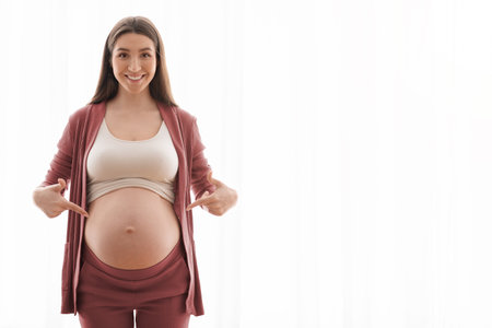 Happy Pregnancy. Positive Young Woman Pointing At Her Naked Pregnant Belly With Two Hands, Standing...