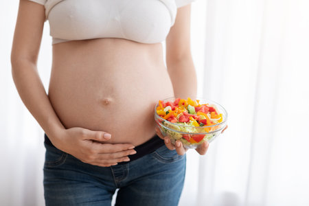 Healthy Food For Future Baby. Unrecognizable Pregnant Woman Holding Bowl With Vegetable Salad And Touching Her Naked Belly, Enjoying Organic Nurtition During Pregnancy, Closeup Shot, Croppedの写真素材