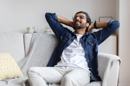 Relaxed smiling arab guy leaning back on couch at home, relaxing after successful day, positive young eastern man resting on sofa with hands behind head, enjoying domestic weekend, free spaceの写真素材