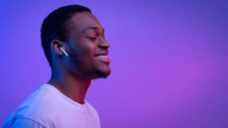 Relaxed African American Man Listening Music In Wireless Airpods Earphones In Neon Light, Smiling Black Guy Wearing Bluetooth Earpods Enjoying Favorite Songs Over Purple Background, Panoramaの写真素材