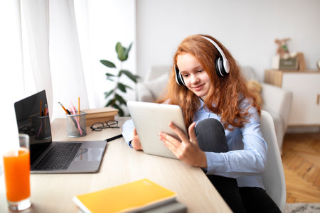 Youth And Gadgets. Cheerful Teenage Girl Watching Videos Or Movie On Digital Tablet, Wearing Wireless Headphones, Relaxing Sitting At Desk At Home, Using Application, Browsing Internetの写真素材