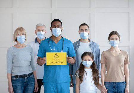 Portrait of diverse people in face masks standing behind African American male doctor with Covid-19...