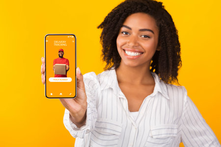 Delivery Tracking. Smiling african american woman holding and showing smartphone with service app to...
