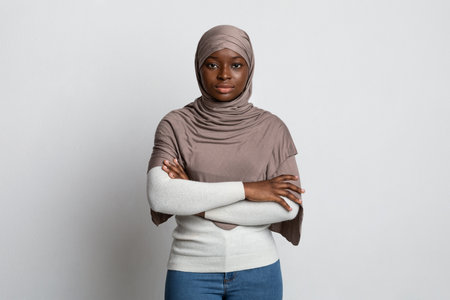 Serious Black Muslim Woman Standing With Folded Arms Over Light Background, Confident African...