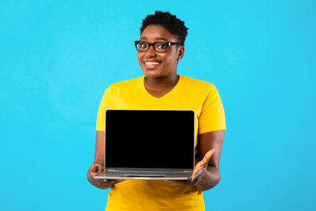Smiling Oversized Black Woman Holding Laptop With Blank Screen Posing Over Blue Studio Background....