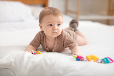 Cute little baby boy or girl playing with toys while laying on bed at home, looking at copy space. Adorable toddler having fun, lying on belly and palying with beanbag. Kids toys, maracas conceptの写真素材