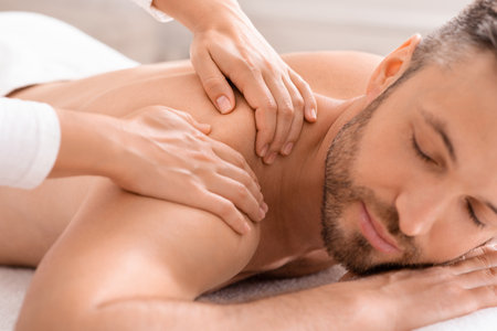 Closeup of bearded middle aged man with closed eyes having relaxed body massage at spa salon. Unrecognizable masseuse rubbing sleeping handsome man shoulders. Stress relief conceptの写真素材