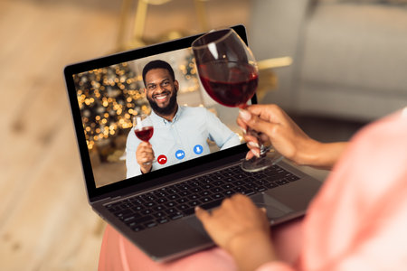 Celebrating Anniversary. Back over the shoulder view of young black woman having a romantic online date with her man, holding glass of red wine and toasting with computer on her lap. Stay Safeの写真素材