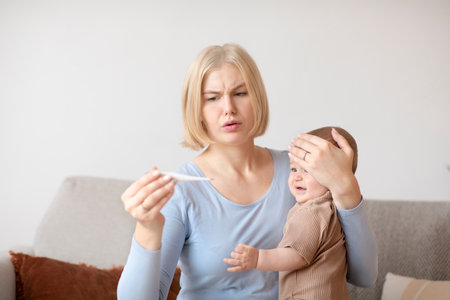 Anxious woman young mother checking temperature to her sick crying baby, using electronic...
