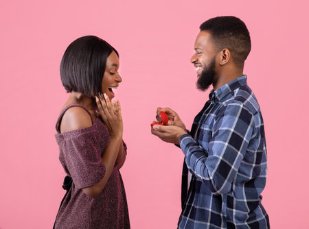Side view of passionate black man proposing to his beloved woman, giving her engagement ring on...