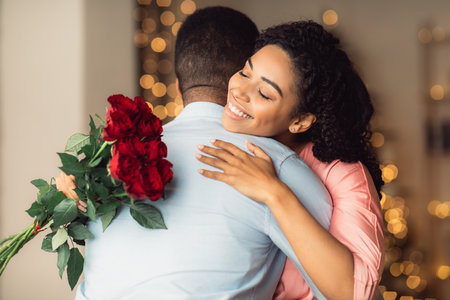 Romantic Relationship. Glad smiling african american woman hugging her man and holding bouquet of red roses. Girlfriend with bunch of flowers embracing boyfriend, celebrating anniversaryの写真素材