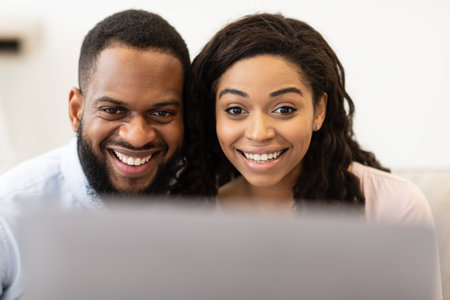 Technology Concept. Closeup portrait of smiling excited black couple using laptop computer, having online video conference with friends or family, watching video or movie spending time at homeの写真素材