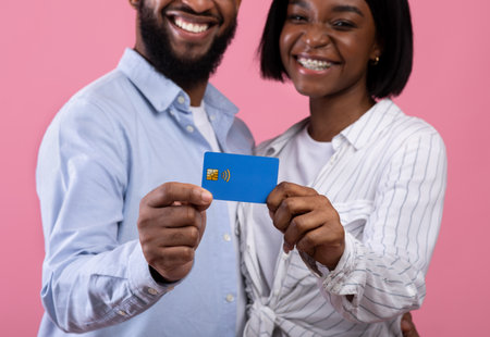 Cropped view of black married couple holding credit card on pink studio background, focus on hands. Romantic guy and his girlfriend promoting contactless shopping for Valentines presentsの写真素材