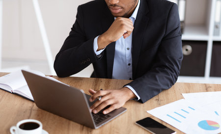 Cropped of black manager in suit working with laptop in office, checking marketing report, modern technologies in business concept. Unrecognizable african american businessman using computerの写真素材