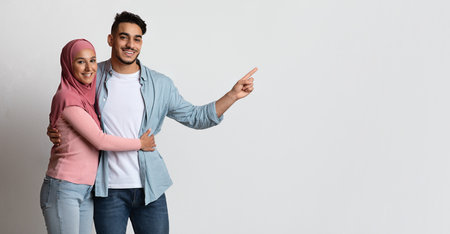 Happy Muslim Couple Embracing And Pointing Aside At Copy Space. Smiling Millennial Arab Spouses...