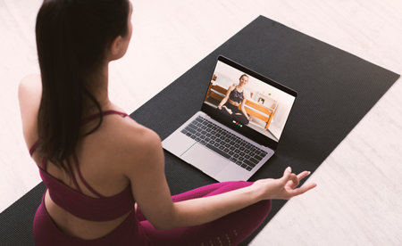 Young woman meditating or doing yoga, following online video instructions from personal trainer, above view. Fit millennial lady sitting in lotus pose on mat, watching web sports tutorial at homeの写真素材