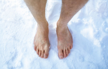 Top view of male feet standing on snow outdoors, cropped. Unrecognizable guy making cold exposure training, overhead shot. Acclimation and healthy lifestyle conceptの写真素材