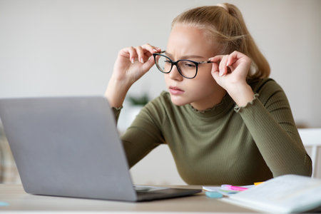 Child vision problems and gadgets concept. Blonde teen girl fixing her glasses while looking at...