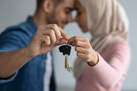 Key in romantic muslim couple hands, closeup. Loving middle eastern man and woman in hijab bonding and holding key from their new house together, selective focus. Moving, real estate conceptの写真素材
