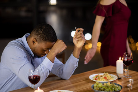 She Said No. Woman Refusing Marriage Proposal From Her Boyfriend At Romantic Dinner In Restaurant And Leaving, Desperate African American Man Sitting At Table Holding Engagement Ring, Croppedの写真素材