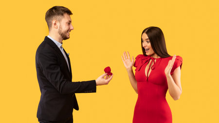 Marry Me Concept. Man Proposing To Woman Giving Her Engagement Ring Standing On Yellow Studio Background. Panoramaの写真素材