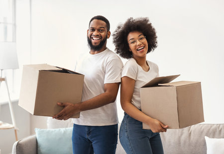 New House. Happy African American Couple Holding Moving Boxes Preparing For Relocation Posing...