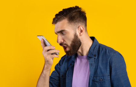 Angry bearded guy shouting at smartphone over orange studio background, panorama. Dissatisfied...