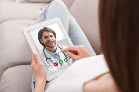 Woman With Digital Tablet Having Online Video Call With Her Doctor While Relaxing On Couch At Home, Unrecognizable Female Getting Virtual Medical Consultation With Physician, Creative Collageの写真素材