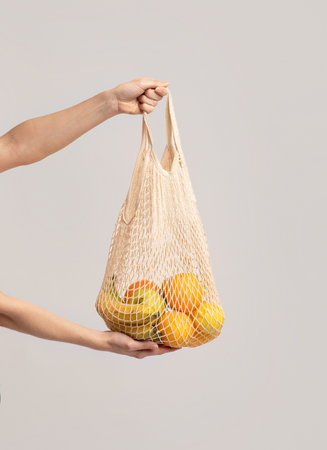 Hands Holding Eco Mesh Bag With Organic Fruits Over Light Studio Background, Unrecognizable Female...