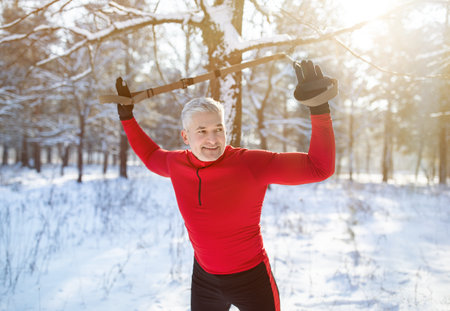 Doing TRX exercises. Senior athletic man training his arms with suspension fitness straps at snowy park. Strong fit guy working out with sports equipment outdoors in winterの写真素材