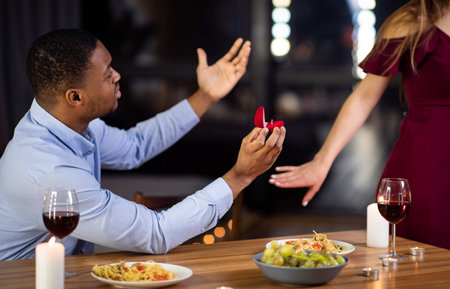 Proposal Rejection. Woman Leaving Black Boyfriend In Restaurant After He Proposed Marriage, Desperate African American Man Begging For Yes Answer, Sitting At Table With Diamond Ring Box In Handの写真素材