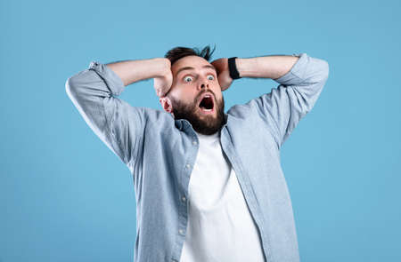 Shocking offer. Extremely surprised young guy shouting OMG in disbelief on blue studio background. Stunned bearded man screaming WOW, cannot believe amazing news, sale, discountの写真素材