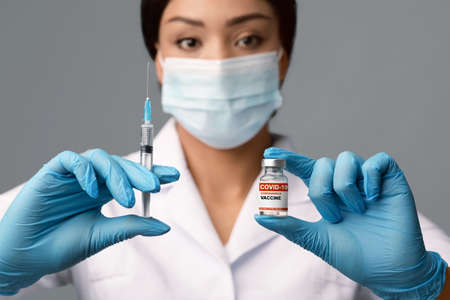 African American Female Doctor Holding Syringe And Vial With Covid-19 Coronavirus Vaccine,...