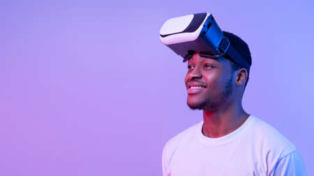Smiling African American Guy Wearing VR Glasses Looking Aside Over Purple Background, Enjoying...