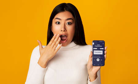 Surprised Asian Woman Holding Smartphone With Opened Voice Translation App On Screen, Using Online...