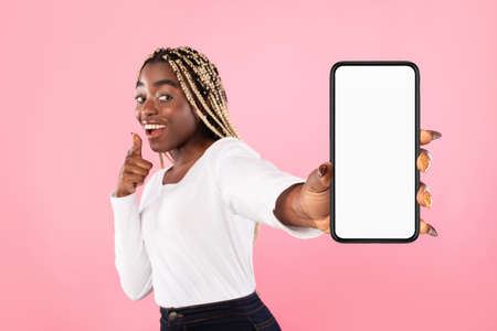 Portrait of cheerful young african american woman holding mobile phone with white blank screen in...