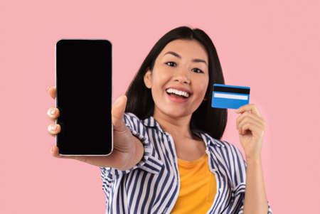 Online Shopping. Portrait of cheerful young asian woman holding credit card in hand and showing...