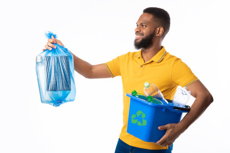 African American Guy Posing With Box Full Of Recycling Plastic And Blue Garbage Bag Standing Over White Background In Studio. Sort And Recycle Your Waste Concept, Side Viewの写真素材