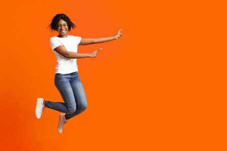 Emotional african american millennial lady smiling and pointing at advertising or announcement....