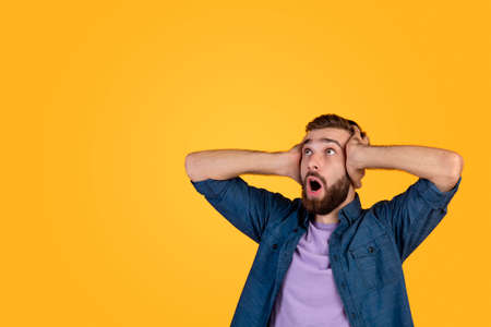 Shocked Caucasian man screaming and grabbing his head in disbelief, looking at blank space on orange...