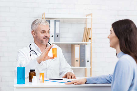 Antidepressants, vitamins, medications, pain relievers. Smiling adult man doctor in white coat shows...