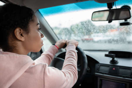 Working as taxi driver in city in bad rainy weather and way to job. Focused young african american...