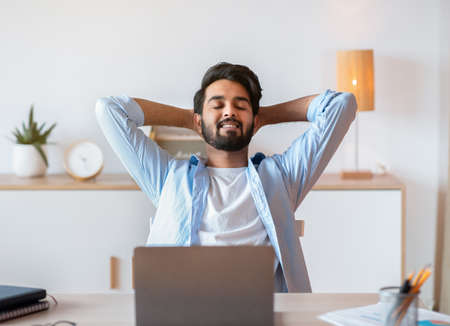 Smiling Arab Freelancer Guy Leaning In Chair, Relaxing At Workplace After Working Remotely On Laptop In Home Office, Happy Successful Eastern Man Enjoying Distant Job Opportunities, Free Spaceの写真素材