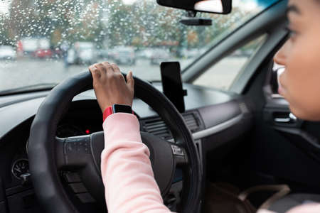 Modern driver with gadgets at work in auto. Concentrated millennial african american female with...