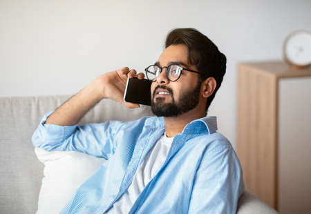 Relaxed Arab Man Talking On Celphone While Resting On Couch At Home In Living Room At Home,...