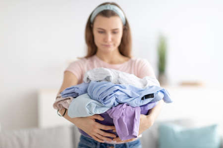 Unhappy millennial housewife with pile of clothes sick and tires of washing or ironing at home,...