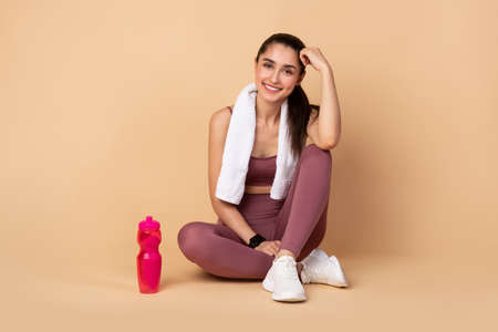 Fitness And Healthy Lifestyle Concept. Happy sporty young woman sitting on the floor with bottle of...
