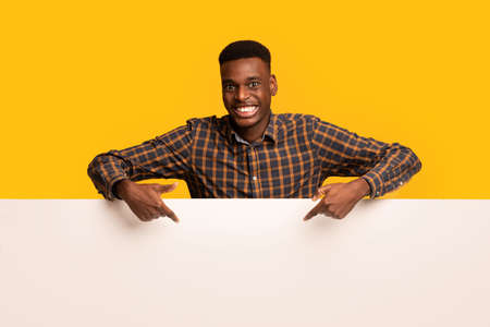 Happy Black Guy Pointing Down At Blank White Advertisement Board, Happy African American Man Demonstrating Copy Space For Your Design, Standing Isolated Over Yellow Backgroundの写真素材