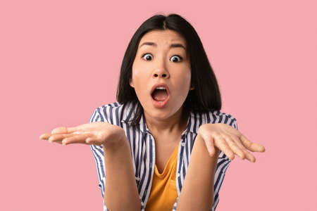 Closeup portrait of surprised amazed young asian woman staring at camera with opened mouth, gesturing, shocked by news or offer, standing isolated on pink studio backgroundの写真素材