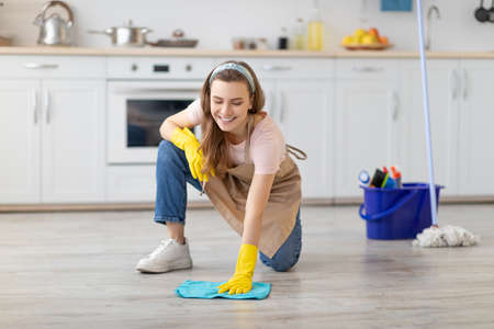 Professional cleaning service. Cheerful young lady in apron and rubber gloves washing floor in...